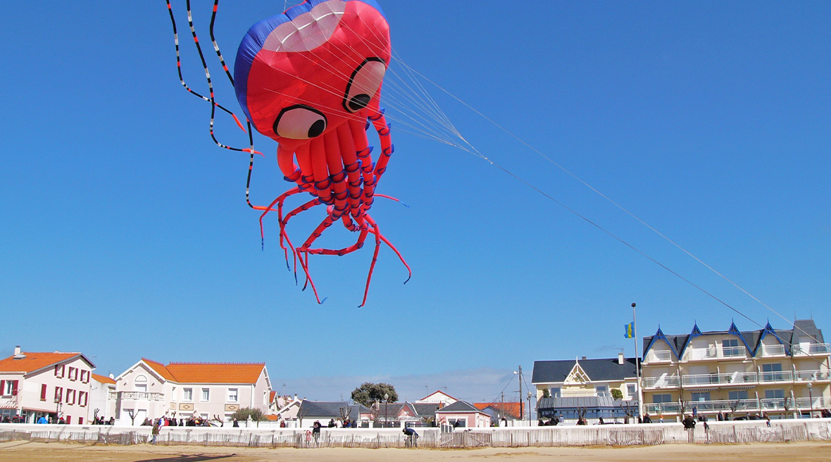 Giant squid kite flying over beach and sea front in cloudless blue sky